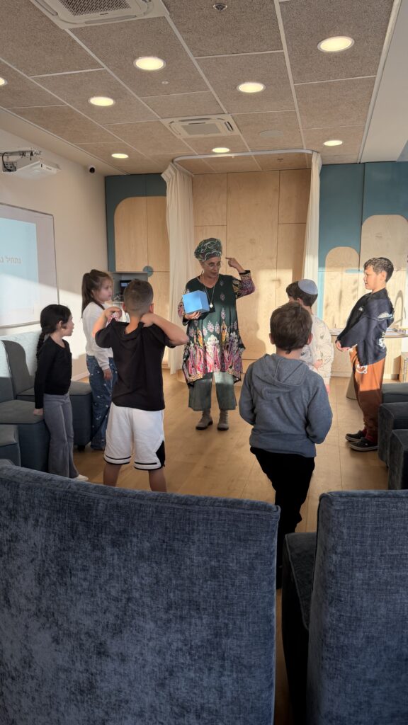 מנחה מובילה פעילות קבוצתית לילדים עם קובייה כחולה במרכז חיוך