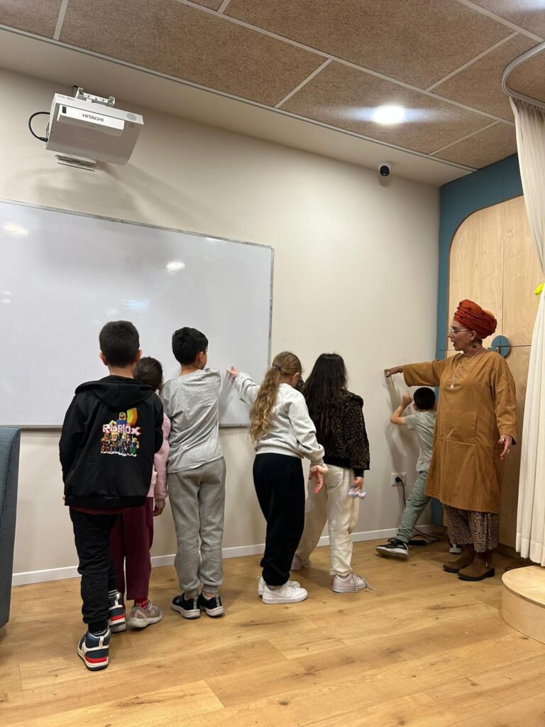 ילדים ומנחה בפעילות קבוצתית למיומנויות חברתיות ליד לוח מחיק
