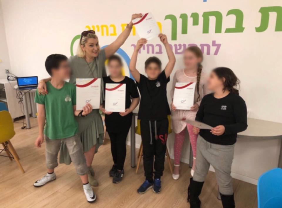 מדריכה וילדים מניפים תעודות סיום במרכז חיוך